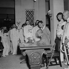 Lt.-Gen. Tanaka signs the Instrument of Surrender while Vice Admiral Fujita awaits his turn, Government House